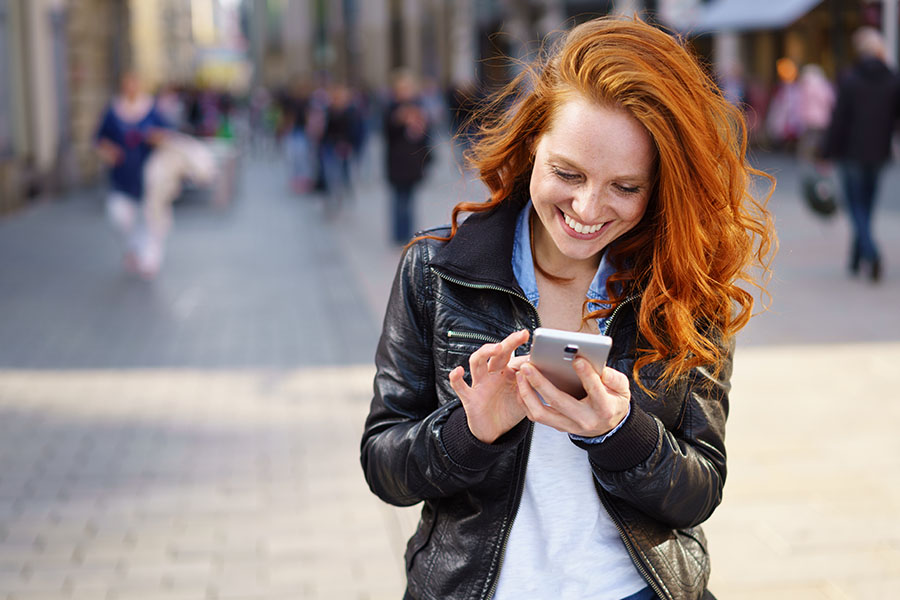 Eine rothaarige Frau schaut auf ein Handy und lächelt.